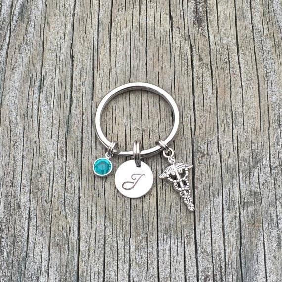 The Birthstone and Initial Caduceus Charm Keychain is a trendy and personalized accessory that combines the symbolic meaning of birthstones with the elegance of a caduceus charm. It is a perfect gift for someone who values their birthstone and appreciates the significance of the caduceus in the medical field.