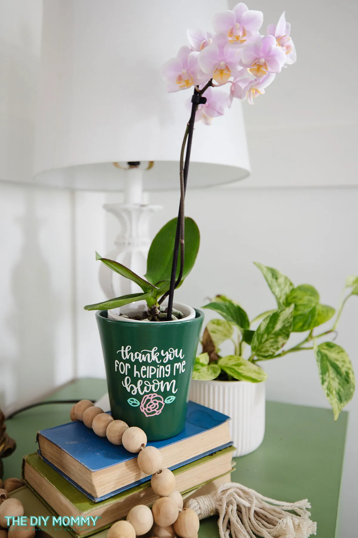 A personalized gardening gift of an orchid in a plant pot. The pot is decorated with a decal that reads &quot;Thank you for helping me bloom.&quot;