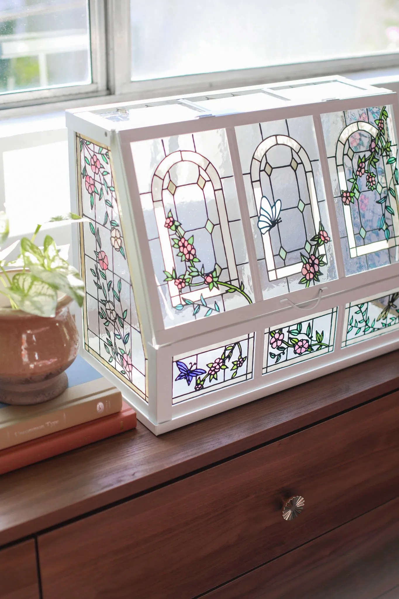 Clear glass greenhouse on a table with faux plants inside