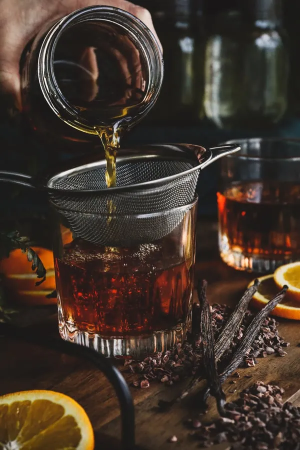 Infused brandy getting strained into drinking glass