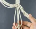 Macrame cord being knotted to make macrame plant hanger.