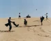 Men in suits play with children on a sand dune.