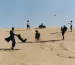 Men in suits play with children on a sand dune.